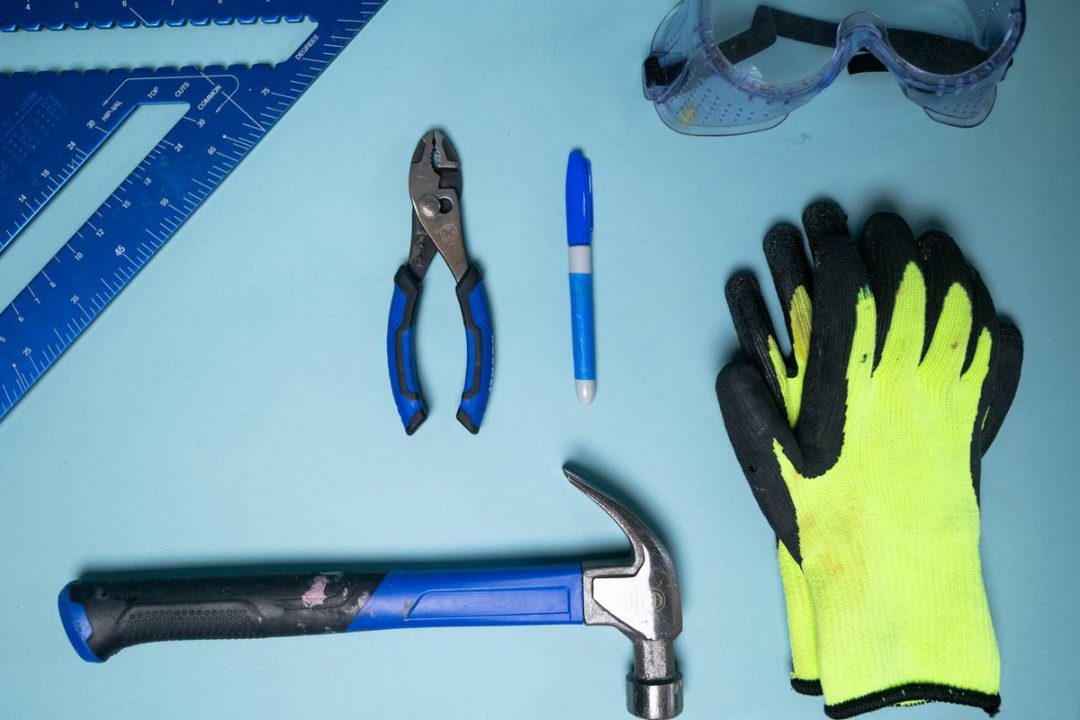 diy home maintenance tips protective: homeowner wearing safety goggles, respirator, and gloves while repairing a sink