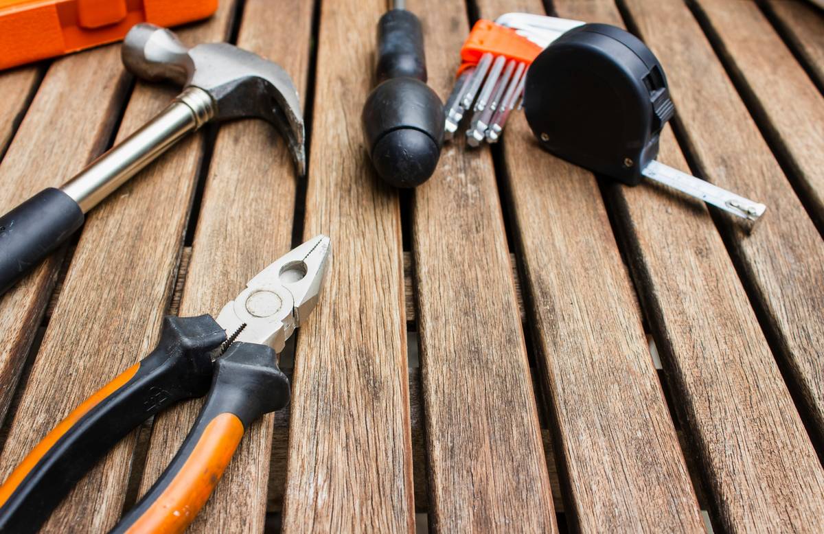 diy home maintenance tips necessary: homeowner wearing gloves and goggles while inspecting a leaky pipe under sink